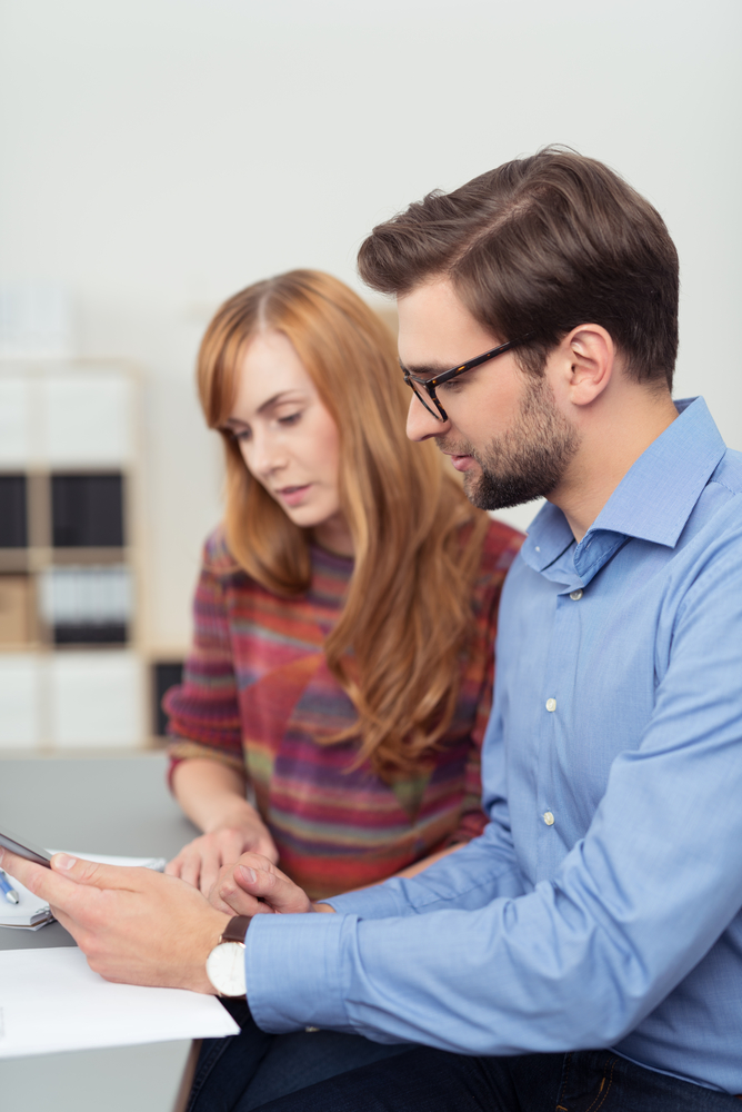 Business man and woman working on a tablet computer as they sit side by side at a desk in the office, closeup side view